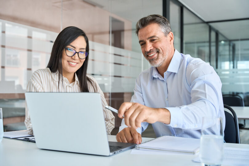 Manager teaching female worker looking at laptop